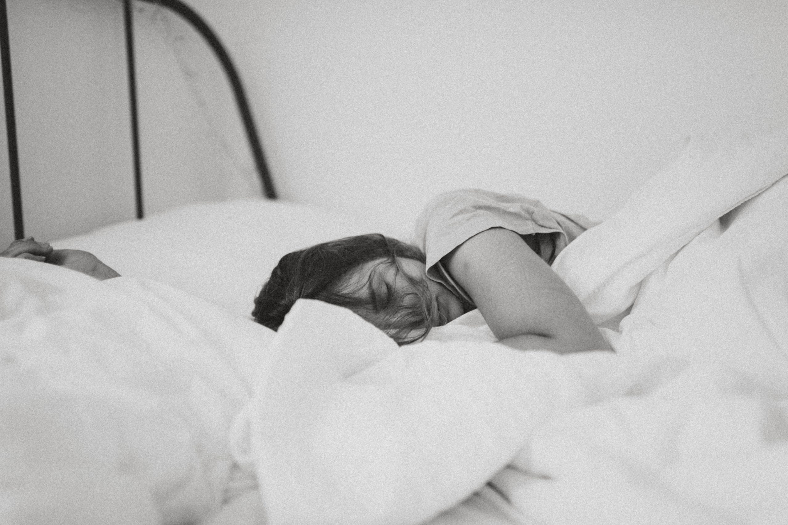 Woman sleeping under large white comforter.